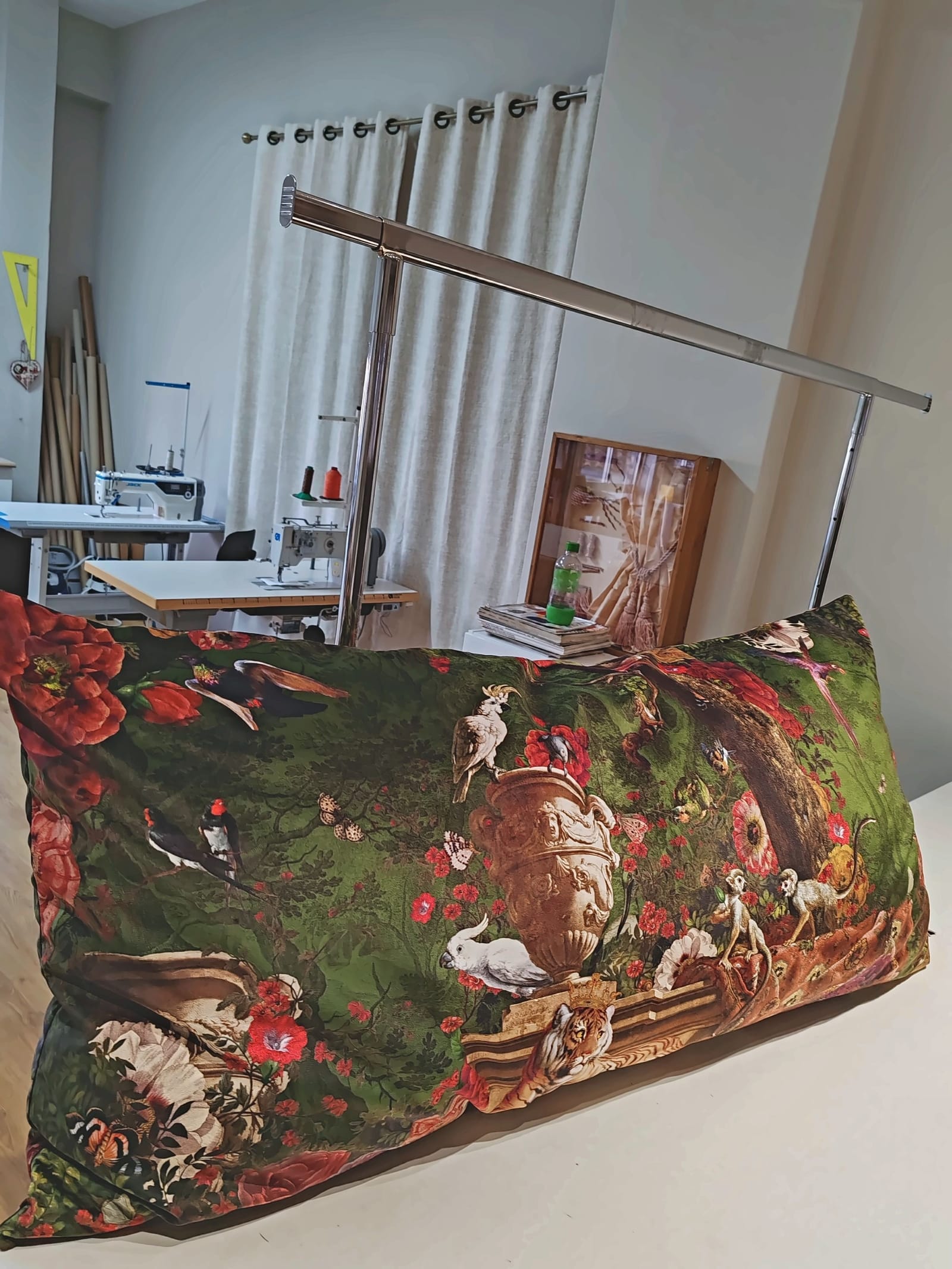 Almofada rectangular estampada com aves, flores e folhagem sobre fundo verde, na mesa do atelier